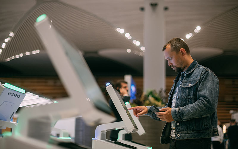 A male passenger at the electronic check-in desk in the departure area of the modern airport terminal.  A young guy checks in for a plane at the screen of a self-service computer kiosk to check in for flights
