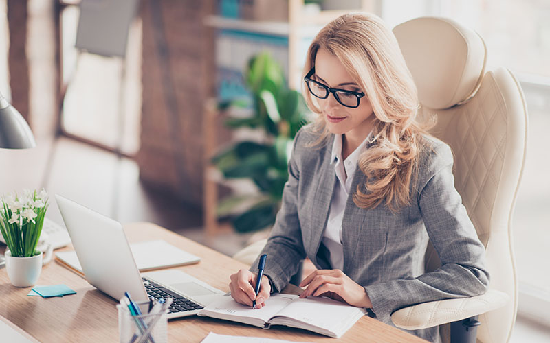 Portrait of stunning busy director sitting at her desk in workstation, workplace, holding pencil in hand, writing a date of conversation in reminder, organizing her day