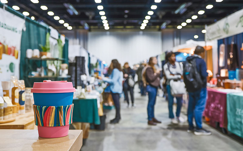 A colorful reusable cup with a rainbow sleeve stands in focus at