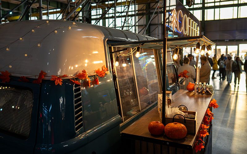 Festively decorated coffee shop in minibus with pumpkins and autumn leaves inside mall market. Cozy seasonal decor, autumn themed market hustle, cozy corner shop on holidays, coffee to go, warm drinks